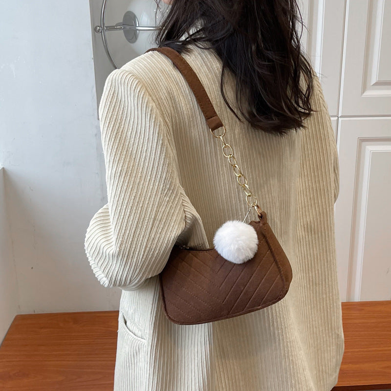 Person wearing a beige ribbed sweater holding a brown handbag with a white pom-pom.