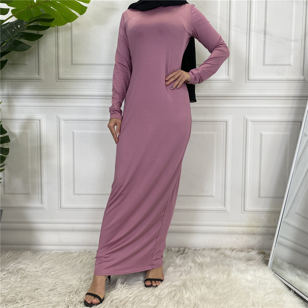 Woman wearing a long mauve dress against a white paneled wall.