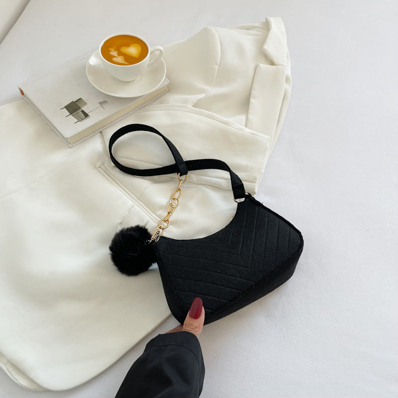 Black handbag with a gold chain on a white surface with a book and cup of coffee.