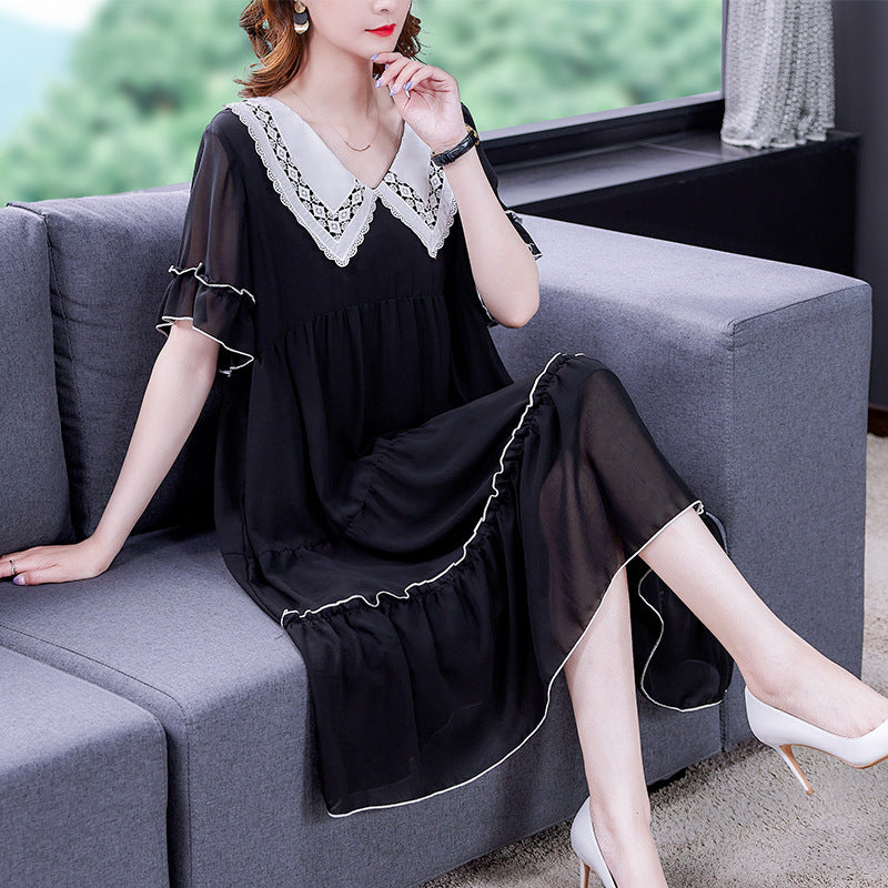Woman in a black dress with white lace details sitting on a gray sofa.