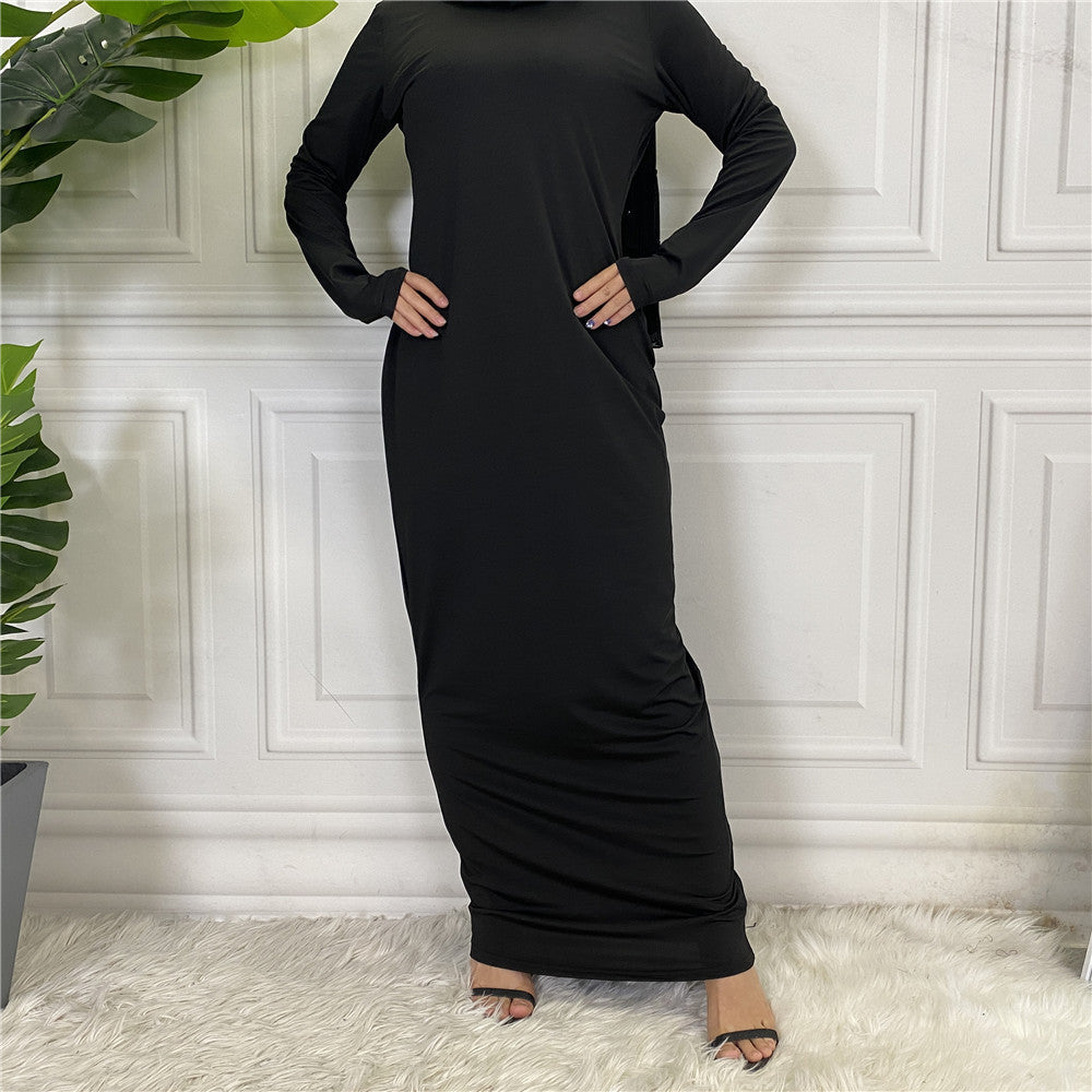 Person wearing a black long-sleeve dress standing against a white paneled wall.
