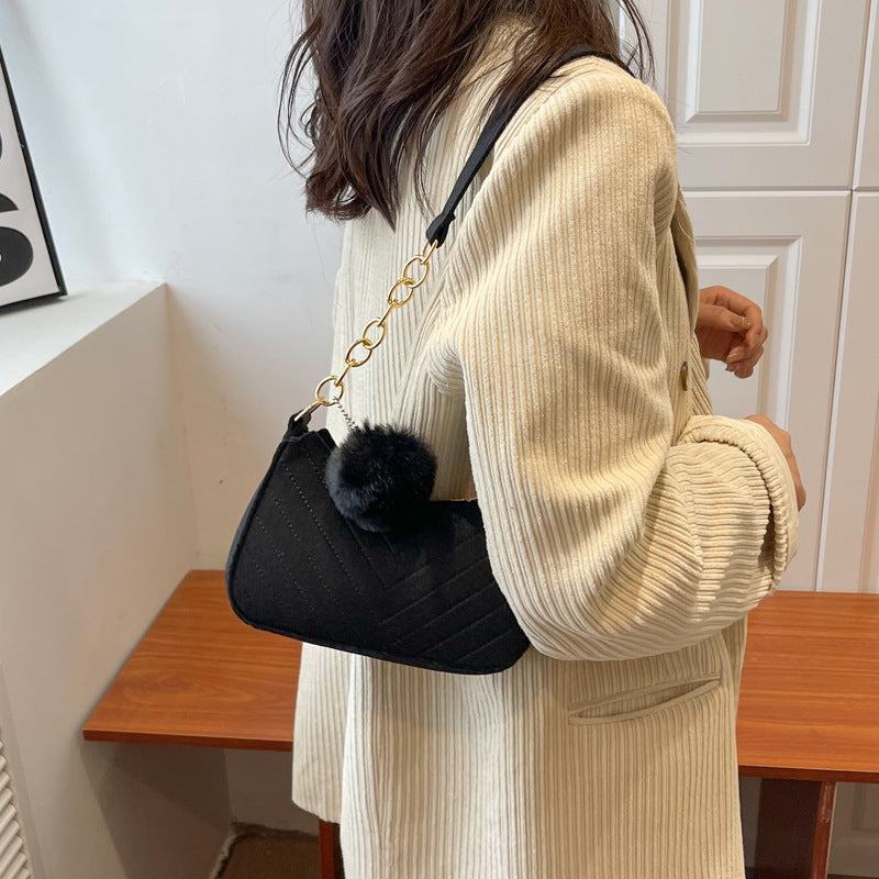 Person wearing a beige sweater holding a black handbag with a pom-pom detail.