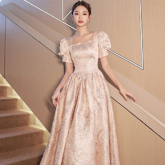 Woman in a beige evening gown standing on a staircase.