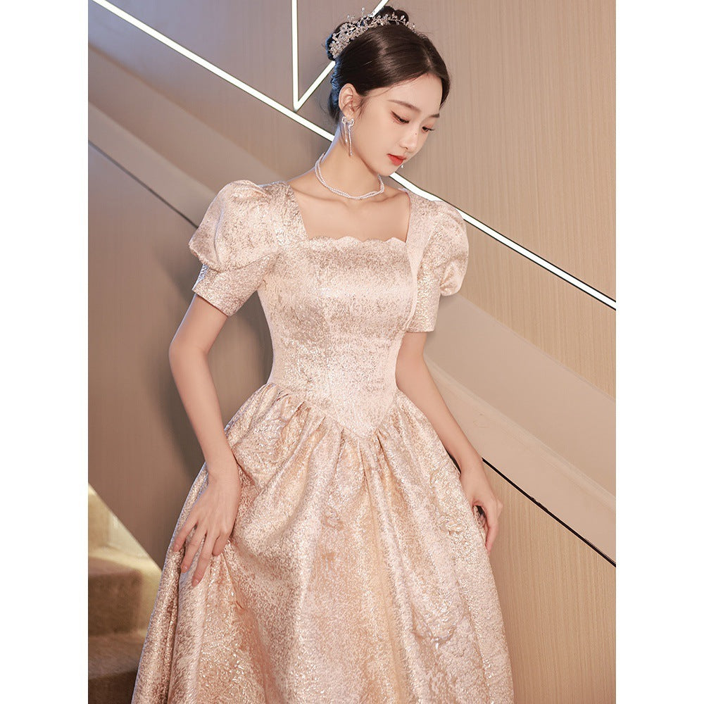 Woman wearing a beige lace dress with a tiara indoors.