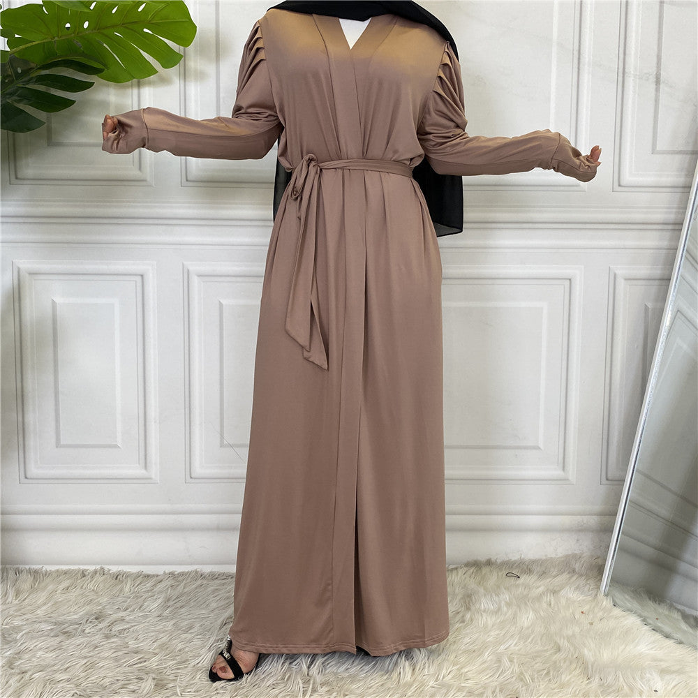 Person wearing a long brown dress with a belt in a room with white paneled walls and a plant.