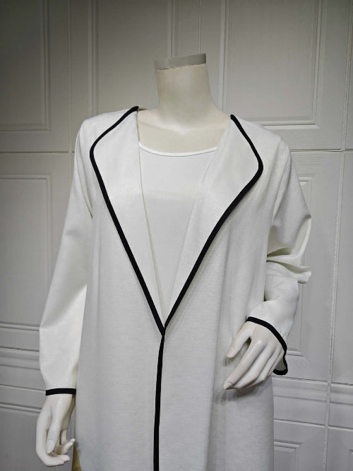 White coat with black trim Modest Floral Style Abaya on a mannequin against a white paneled wall.