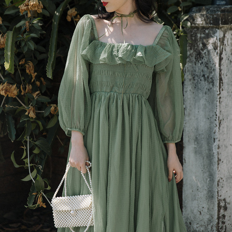 Women's Temperament Fashion Dresses. Woman wearing a green dress with ruffled details, standing against a textured wall and plant background.