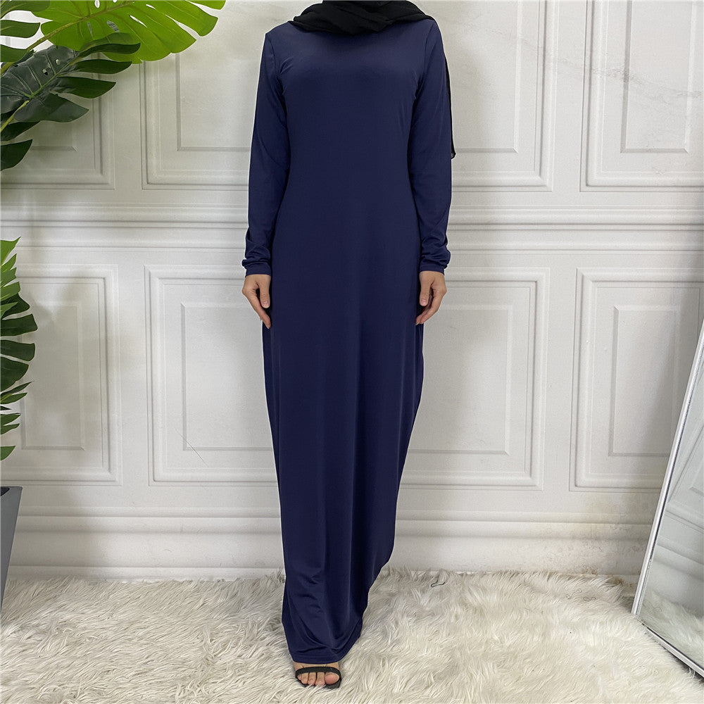 Person wearing a long navy dress standing against a white paneled wall.