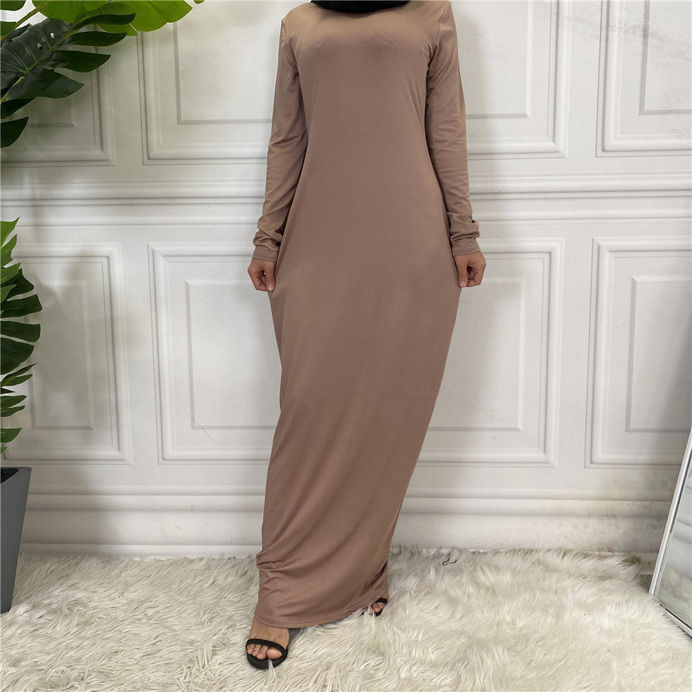 Person wearing a long brown dress standing against a white paneled wall.