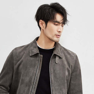 Man wearing a gray jacket over a black shirt with white pants on a light gray background