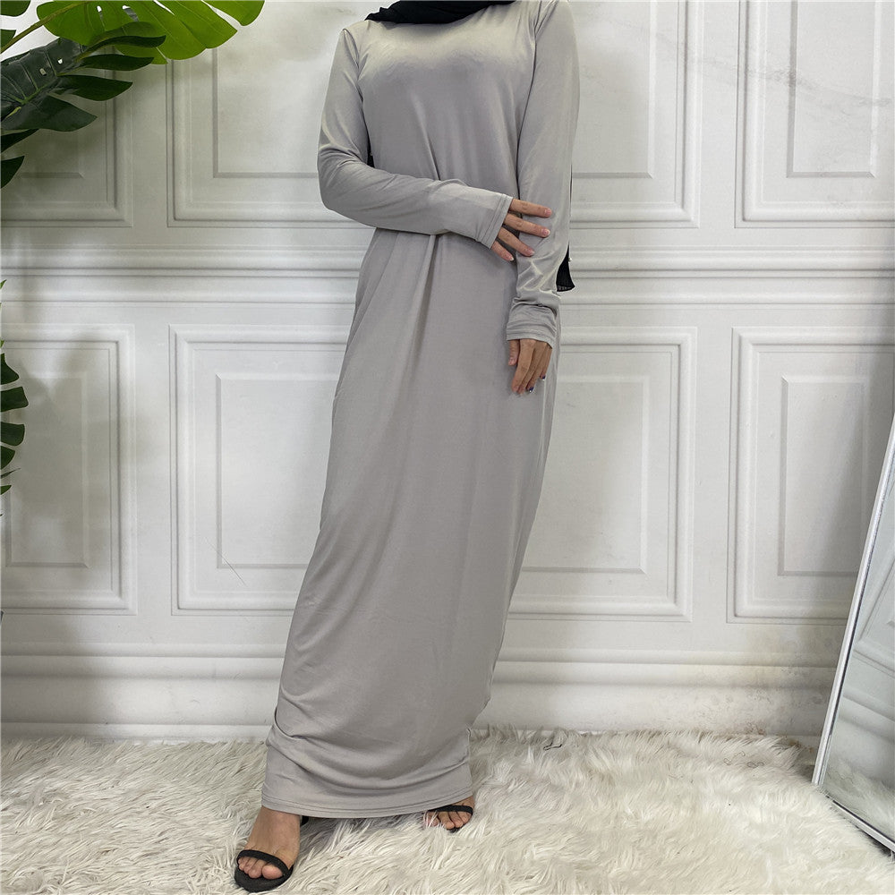 Woman wearing a long gray dress against a white paneled wall.