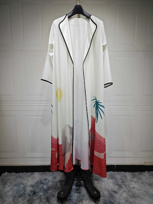 Long white Modest Floral Style Abaya with black trim and colorful design on a hanger against a white paneled wall.