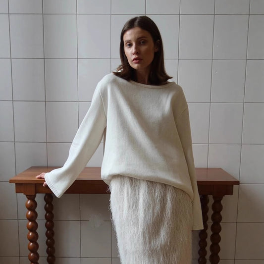 Woman wearing a white sweater and skirt standing against a tiled wall.