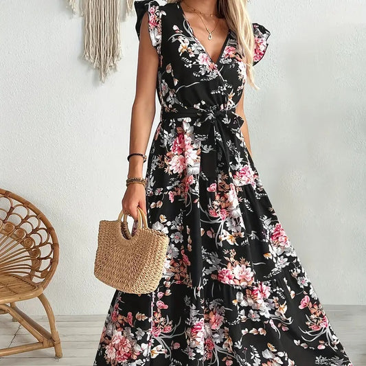 Woman wearing a black floral dress holding a straw bag against a white wall.